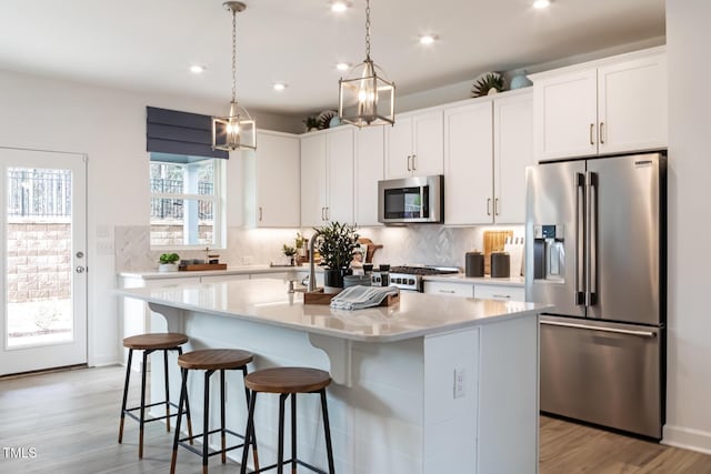 kitchen with a kitchen island with sink, hanging light fixtures, light hardwood / wood-style flooring, appliances with stainless steel finishes, and white cabinetry