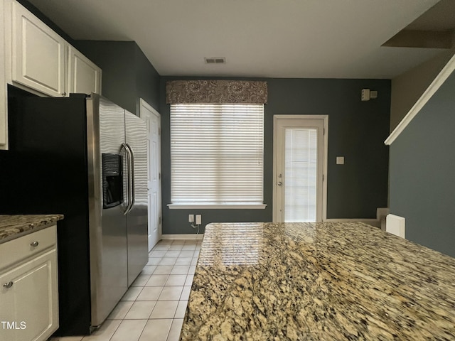 kitchen with light tile patterned flooring, stainless steel fridge with ice dispenser, plenty of natural light, stone counters, and white cabinets