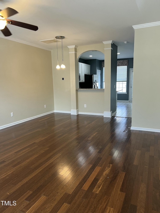 unfurnished living room with decorative columns, ornamental molding, ceiling fan, and dark hardwood / wood-style flooring