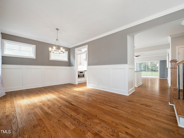 unfurnished dining area featuring wood-type flooring, ceiling fan with notable chandelier, and ornamental molding