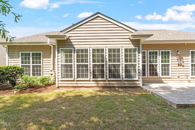 rear view of house featuring a yard, a patio, and a shingled roof