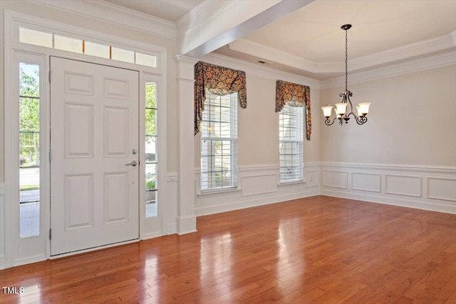 entryway featuring ornamental molding, wood finished floors, a chandelier, and a wainscoted wall