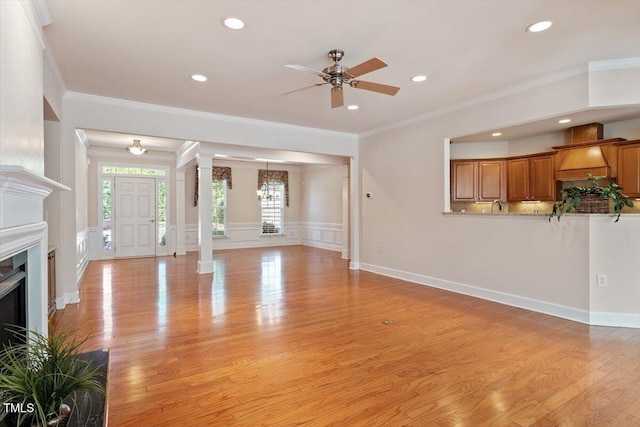 unfurnished living room with crown molding, ceiling fan, decorative columns, and light wood finished floors