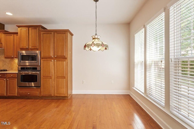 kitchen with stainless steel appliances, baseboards, brown cabinetry, and light wood-type flooring