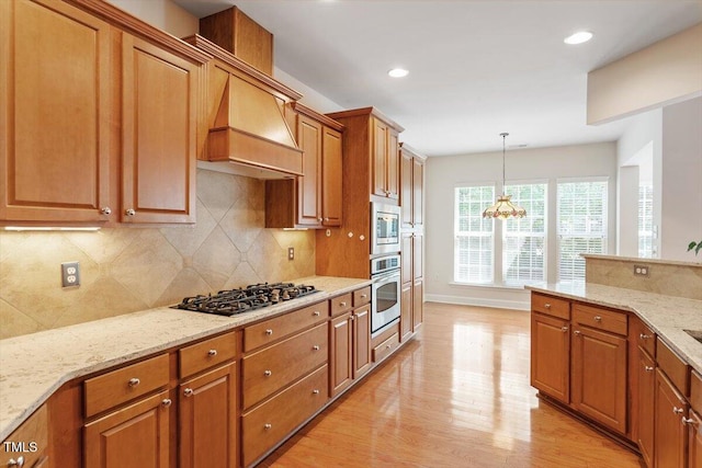 kitchen featuring backsplash, light stone countertops, brown cabinets, light wood finished floors, and stainless steel appliances