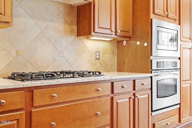 kitchen with light stone counters, appliances with stainless steel finishes, brown cabinets, and tasteful backsplash