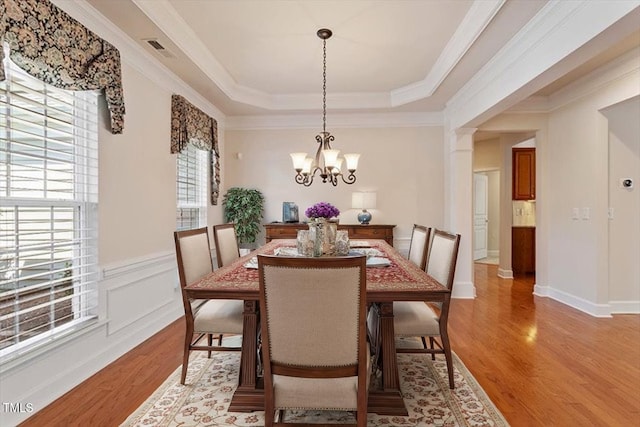 dining space with light wood-style floors, a tray ceiling, a chandelier, and visible vents
