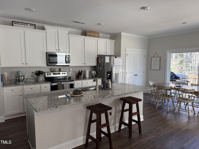 kitchen featuring white cabinets, appliances with stainless steel finishes, a kitchen island with sink, and a kitchen breakfast bar