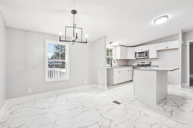 kitchen with appliances with stainless steel finishes, a kitchen island, sink, white cabinetry, and hanging light fixtures