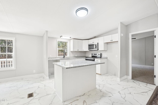 kitchen with sink, stainless steel appliances, a kitchen island, light stone counters, and white cabinets