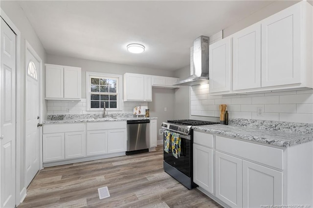 kitchen featuring white cabinets, wall chimney range hood, sink, and appliances with stainless steel finishes