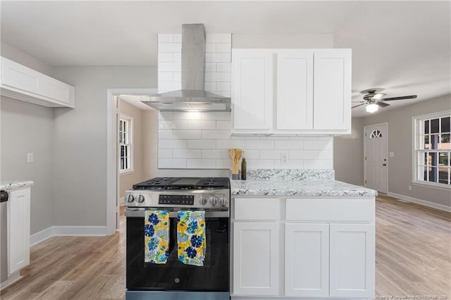 kitchen featuring decorative backsplash, ceiling fan, wall chimney range hood, white cabinets, and stainless steel range with gas cooktop