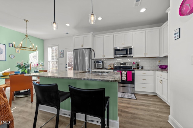 kitchen with dark stone countertops, a chandelier, a center island with sink, white cabinets, and appliances with stainless steel finishes