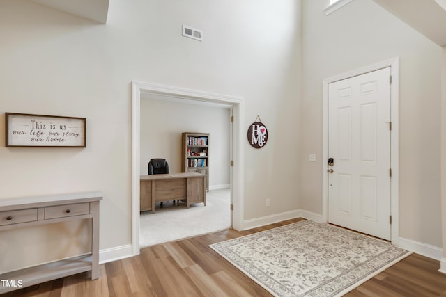 foyer entrance featuring a towering ceiling and light wood-type flooring