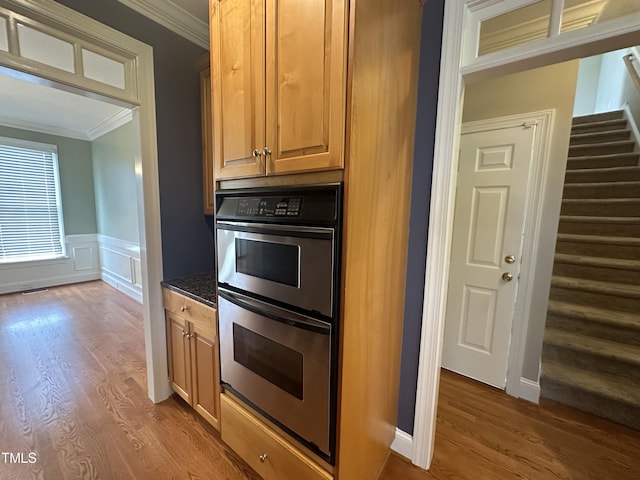 kitchen with wood-type flooring, stainless steel double oven, dark stone counters, and ornamental molding