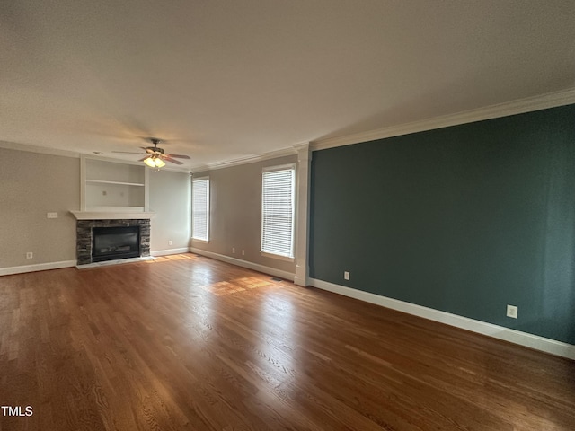 unfurnished living room with ceiling fan, a stone fireplace, built in features, and crown molding