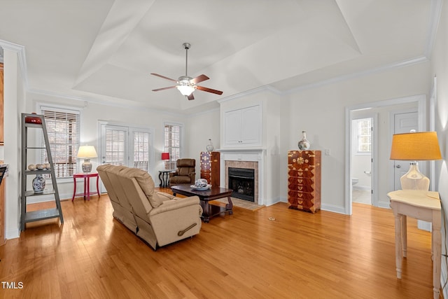 living room featuring ceiling fan, light hardwood / wood-style floors, a raised ceiling, and a fireplace