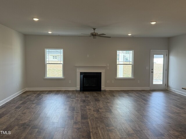 unfurnished living room with dark wood finished floors, a fireplace, plenty of natural light, and baseboards