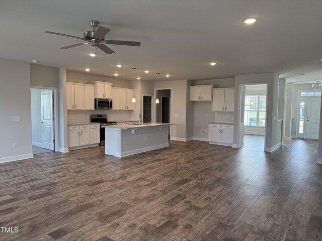 kitchen featuring dark wood finished floors, stainless steel appliances, white cabinets, a sink, and an island with sink