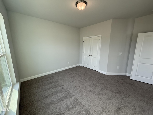 unfurnished bedroom with baseboards, dark colored carpet, and a closet