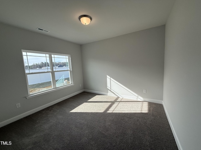 spare room featuring dark carpet, visible vents, and baseboards