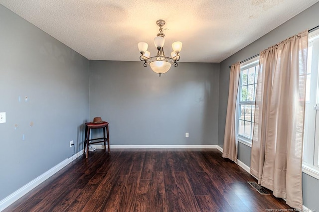 unfurnished room with dark hardwood / wood-style flooring, a textured ceiling, and an inviting chandelier