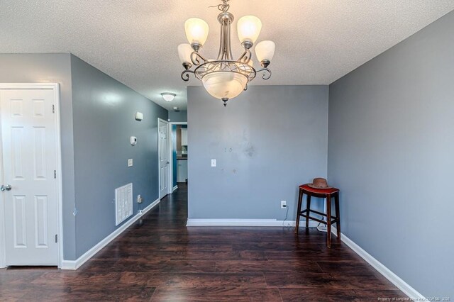 unfurnished dining area featuring a chandelier, a textured ceiling, and dark hardwood / wood-style flooring