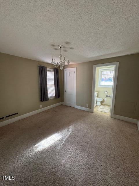 unfurnished bedroom featuring a textured ceiling, carpet floors, an inviting chandelier, and ensuite bath