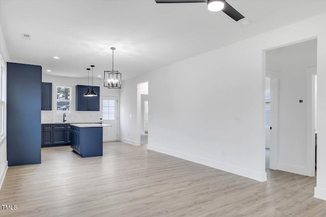 kitchen with backsplash, sink, hanging light fixtures, light hardwood / wood-style floors, and a kitchen island