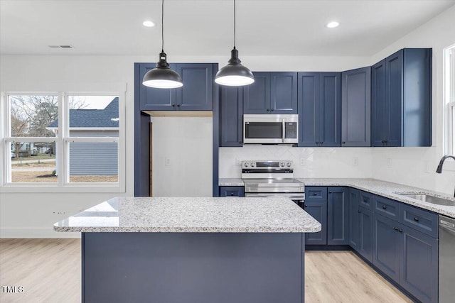 kitchen with light stone countertops, appliances with stainless steel finishes, sink, decorative light fixtures, and a center island