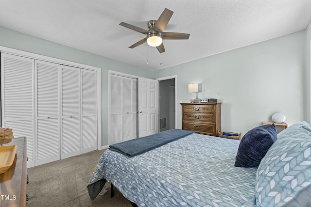 carpeted bedroom with multiple closets, a textured ceiling, and ceiling fan