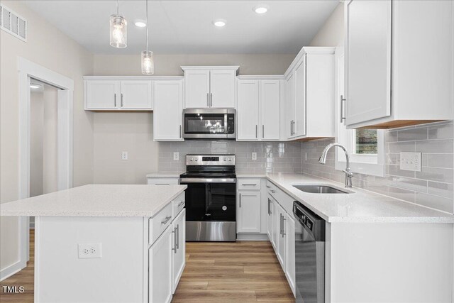 kitchen featuring stainless steel appliances, sink, white cabinets, a center island, and hanging light fixtures