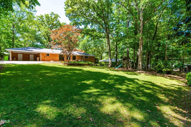 5205 Rembert Dr, Raleigh, NC 27612 - view of green lawn with driveway, a playground, and a carport