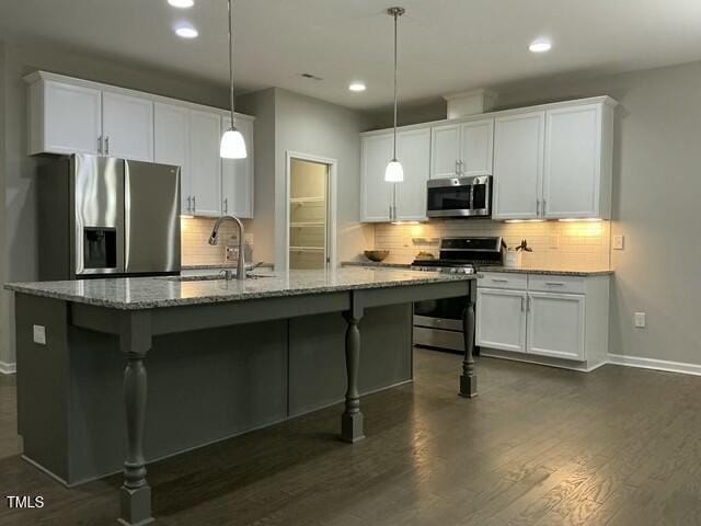 kitchen featuring stainless steel appliances, hanging light fixtures, a center island with sink, and white cabinets