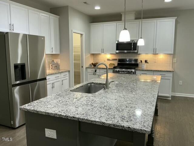 kitchen with sink, appliances with stainless steel finishes, white cabinets, a center island with sink, and decorative light fixtures