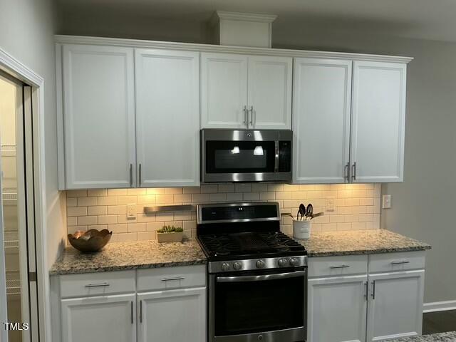 kitchen featuring appliances with stainless steel finishes, backsplash, white cabinets, and light stone counters