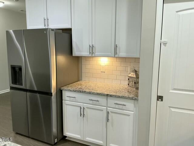 kitchen with stainless steel fridge, light stone countertops, and white cabinets