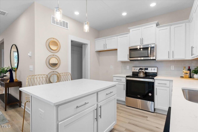 kitchen featuring decorative backsplash, white cabinetry, hanging light fixtures, and appliances with stainless steel finishes