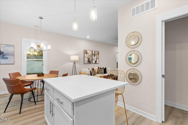 kitchen featuring decorative light fixtures, light hardwood / wood-style floors, white cabinetry, and a kitchen island