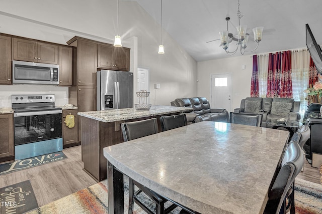 kitchen with pendant lighting, a center island, high vaulted ceiling, an inviting chandelier, and appliances with stainless steel finishes