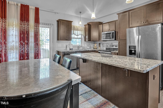 kitchen with light stone countertops, a center island, hanging light fixtures, and appliances with stainless steel finishes