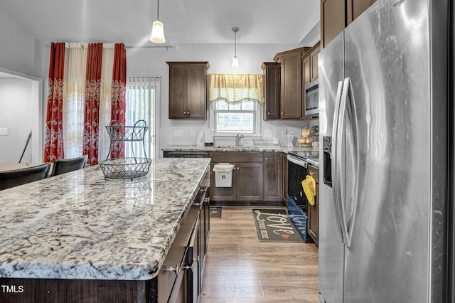 kitchen with pendant lighting, a center island, sink, appliances with stainless steel finishes, and light stone counters