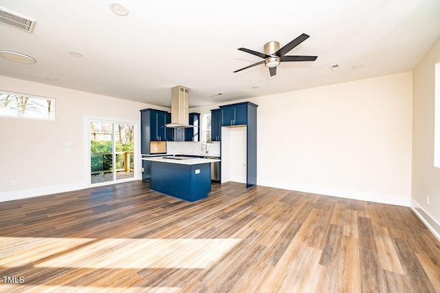 kitchen featuring island range hood, blue cabinetry, hardwood / wood-style floors, a kitchen island, and a breakfast bar area