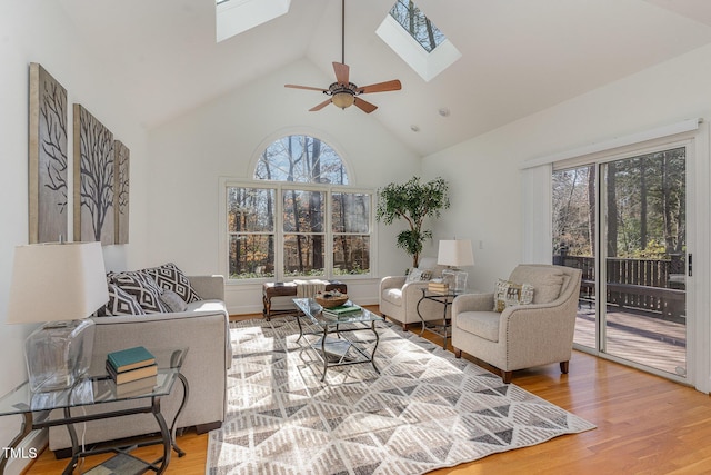 living room featuring wood-type flooring, ceiling fan, and vaulted ceiling with skylight