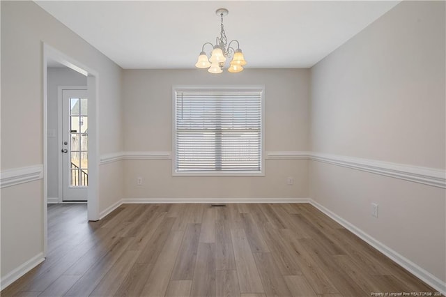 spare room with light hardwood / wood-style floors and an inviting chandelier