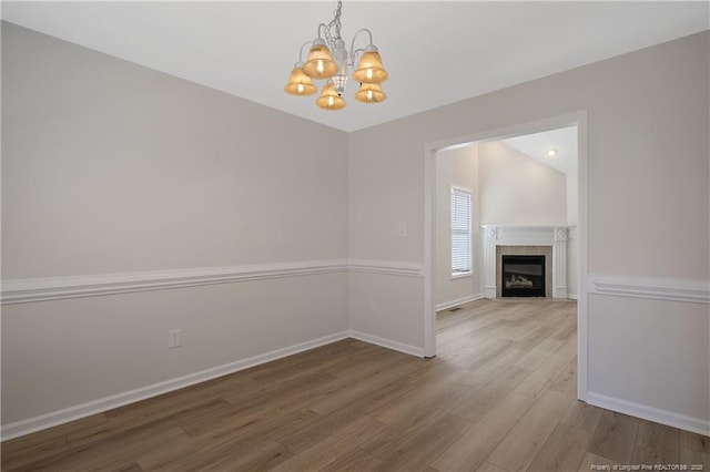 unfurnished dining area with a tile fireplace, hardwood / wood-style floors, and an inviting chandelier