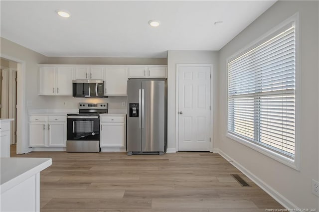 kitchen with white cabinets, appliances with stainless steel finishes, and light hardwood / wood-style flooring