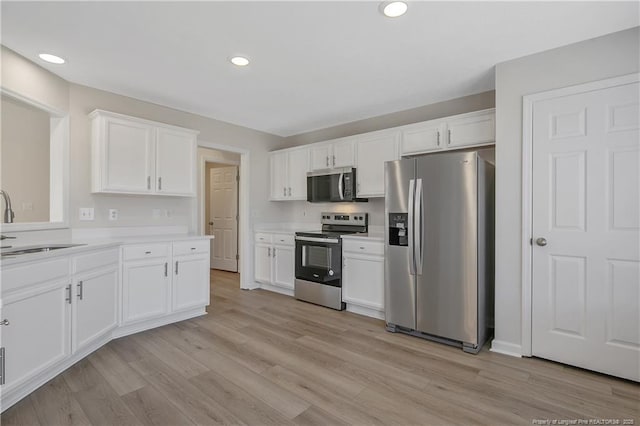 kitchen with sink, white cabinets, stainless steel appliances, and light hardwood / wood-style flooring