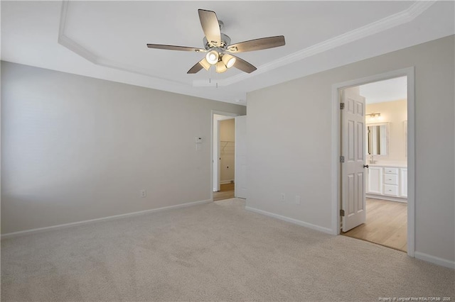 unfurnished bedroom featuring ensuite bath, ceiling fan, crown molding, light colored carpet, and a tray ceiling