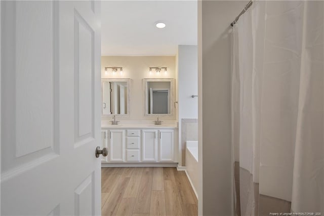 bathroom featuring wood-type flooring, vanity, and a relaxing tiled tub